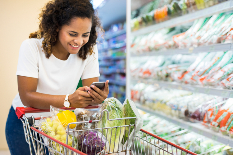 Woman shopping vegetables at the supermarket while researching price comparisons.