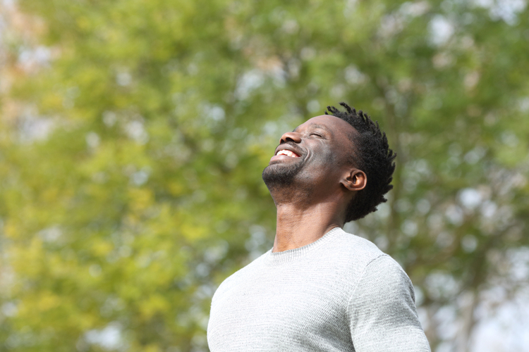 Happy African American man in the park breathing fresh air on a sunny day.