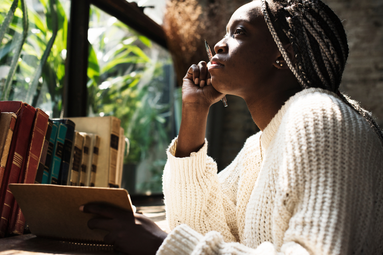 Portrait of black woman with dreadlocks hair writing on her diary.
