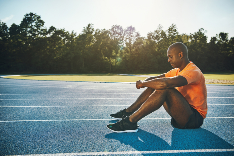 Male athlete in sportswear sitting alone on a running track showing mental health in athletes.