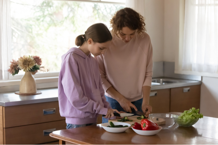 Mother teach teenage daughter cooking healthy food at home kitchen.