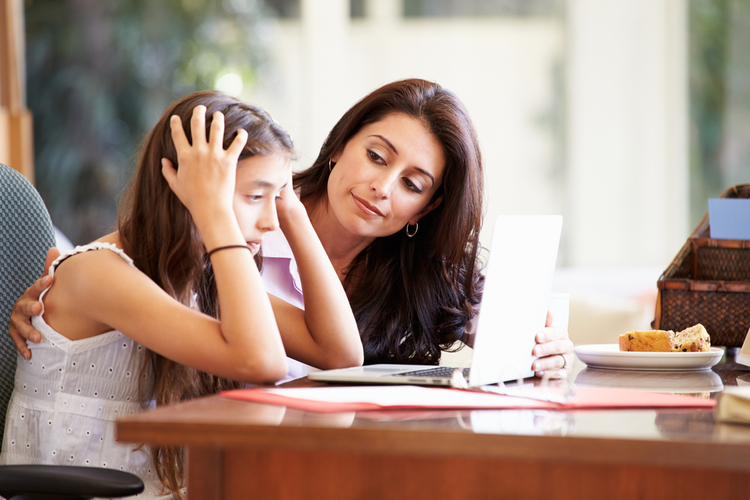 Mother helping stressed teen daughter looking at a laptop.