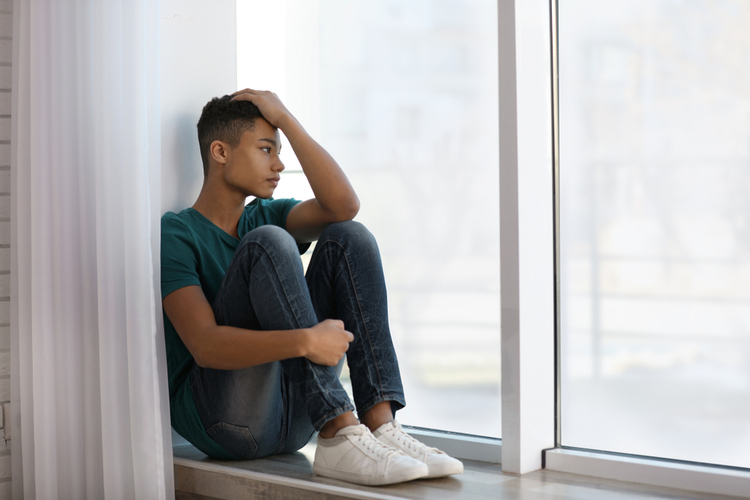 A boy sitting alone near a window suffering from teen depression.