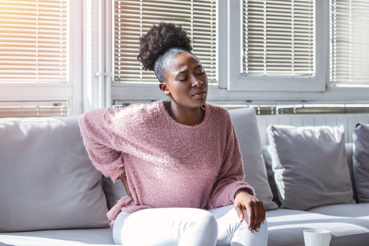 Black woman suffering from backache at home.