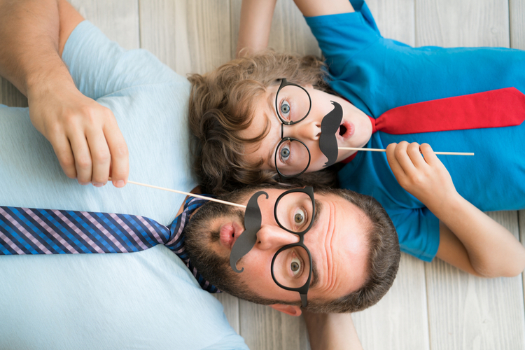 Funny man and kid with fake mustache for no shave november. Happy family playing in home. Movember concept