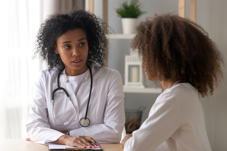 Serious African American female doctor talk to teenage girl sitting at table