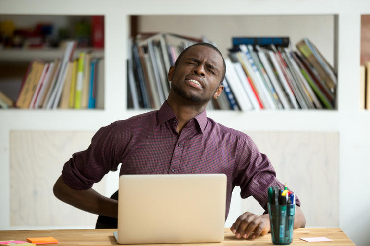 African-american man touching back sitting at desk feeling sudden backache,