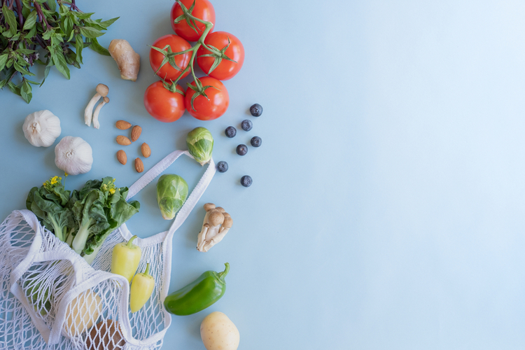 Cotton eco net bag with fresh vegetables and fruit on flat lay blue background.