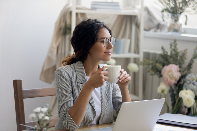 Smiling young Caucasian businesswoman in glasses drink coffee enjoy morning in home office