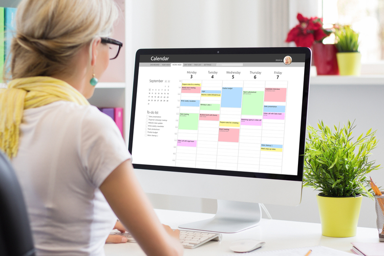 Woman using calendar app on computer in office.