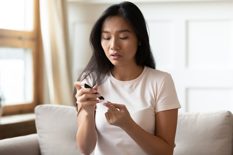 Asian Diabetes Patient Woman Sit on Couch Pinch Finger Measure Blood Sugar Level at Home