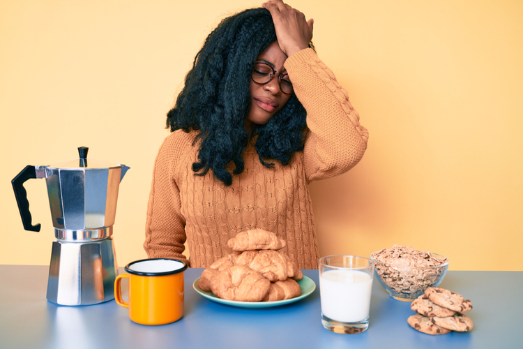 Woman sitting on the table eating breakfast feeling stressed out.