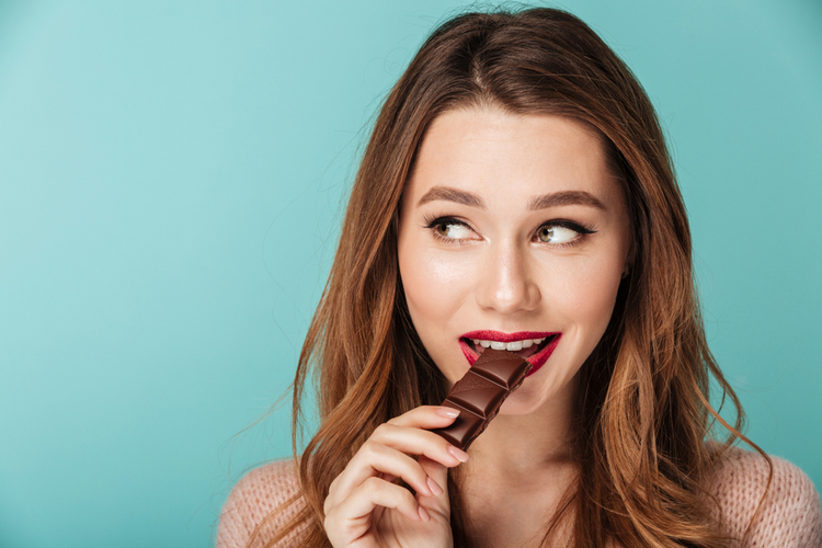 Portrait of a smiling woman eating hu kitchen healthy snacks chocolate bar.