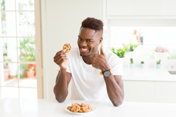 Man eating chocolate chips cookies happy with big smile doing ok sign.