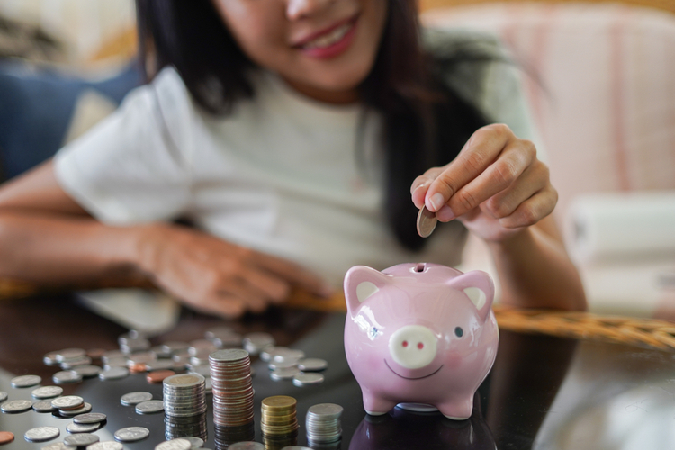 Woman is smiling and hand putting coin into piggy bank, Finance or Savings concept.