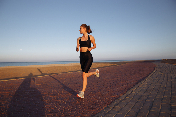 girl runner in a black tracksuit and sneakers runs by the sea during sunset
