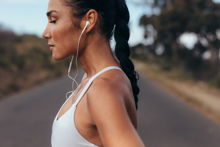 Woman in fitness gear standing on a road listening to podcast