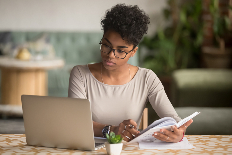 African american businesswoman looking at laptop holding book learning