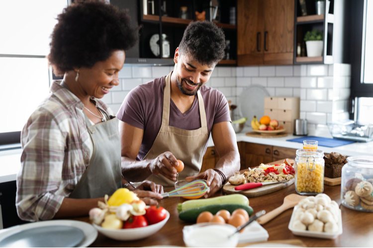 Beautiful young couple is talking and smiling while cooking in kitchen at home.