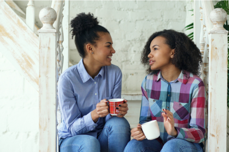 Two african american curly girls sistres sitting on stairs have fun laughing and chatting together