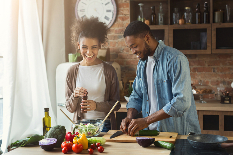 Laughing black couple preparing healthy salad together in loft kitchen