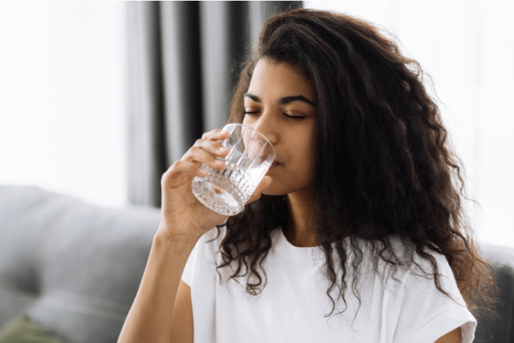 woman drinks a glass of water while sitting on the sofa