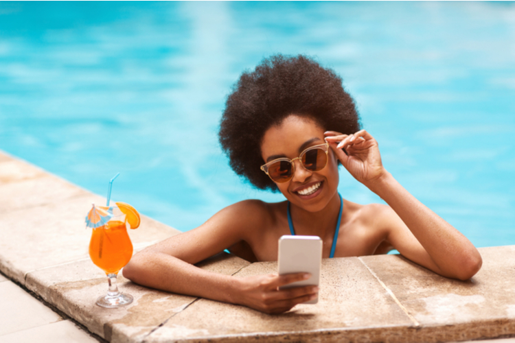 girl with tropical cocktail browsing internet on smartphone at outdoor swimming pool