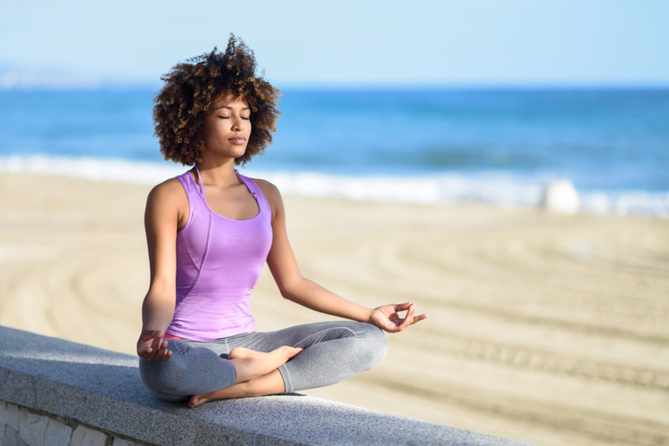 woman doing yoga asana in the beach with eyes closed.