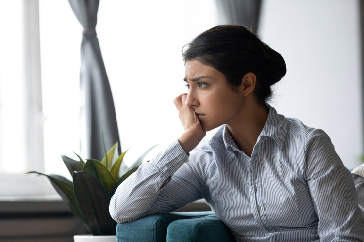 Upset depressed young Indian woman sit on couch at home