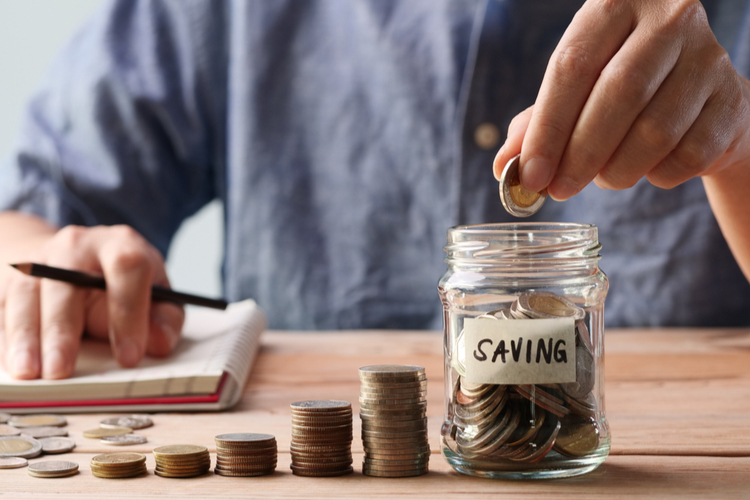 Saving Money. Man hand putting coins in a glass jar.