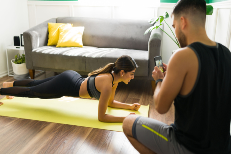 A man taking a picture with a phone of his fitness sporty girlfriend doing a plank exercises
