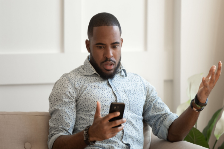 Man sitting on sofa holds cellphone read e-mail sms feels shocked received terrified news