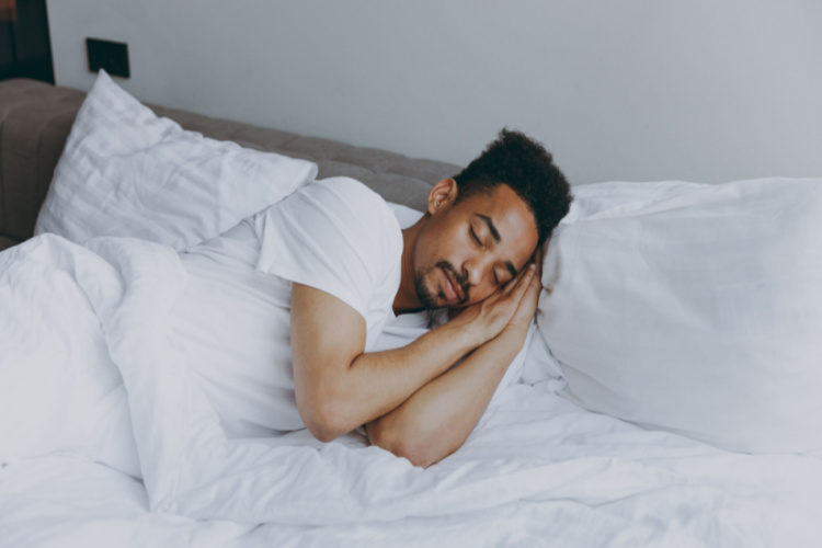 Man 20s wear nightwear sleep with folded hands under cheek lying in bed 