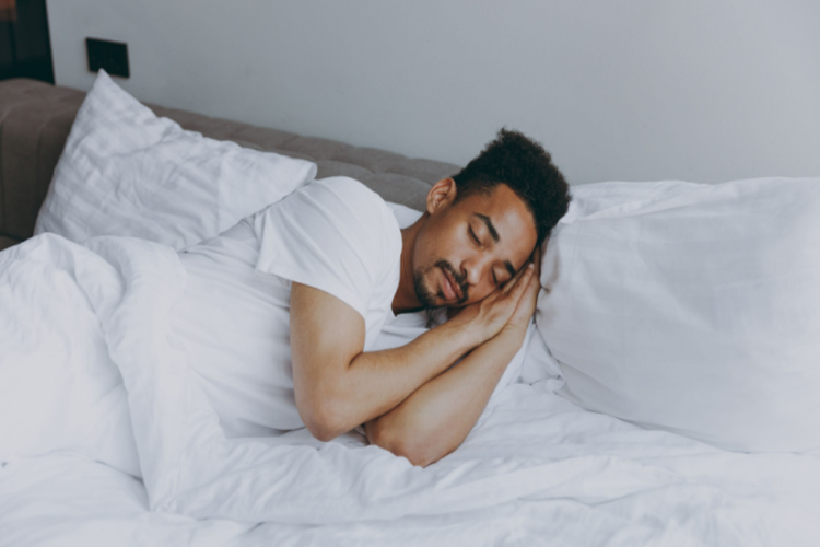 Man 20s wear nightwear sleep with folded hands under cheek lying in bed