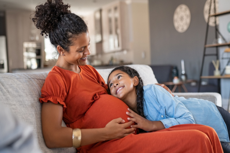 daughter hugging belly of her expecting mother at home