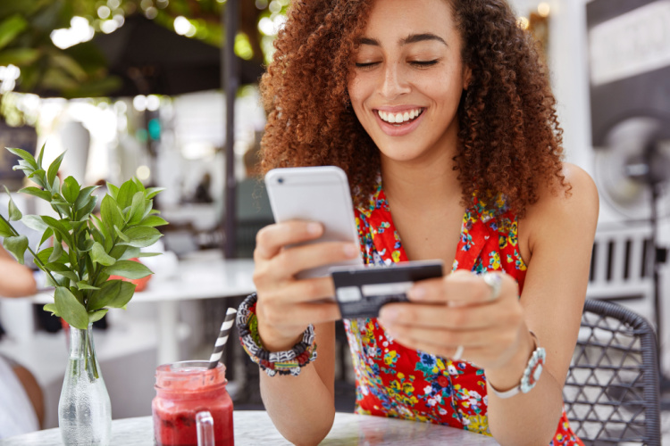 female with cheerful expression, holds smart phone and credit card.