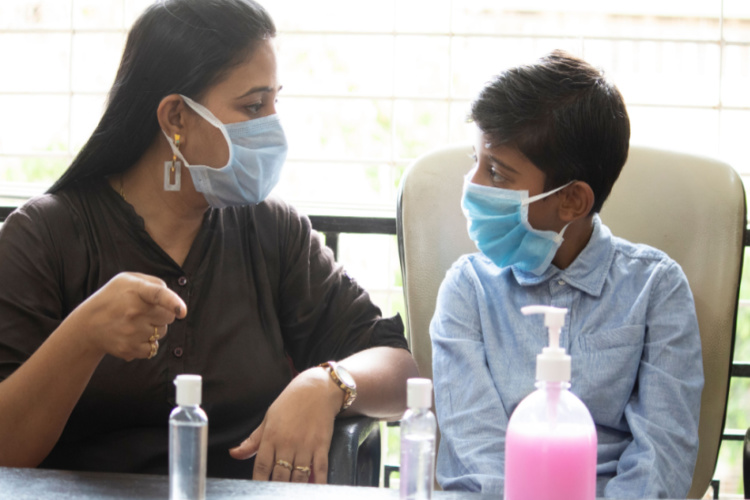 mother wearing face mask explaining her son how to use hand sanitizer