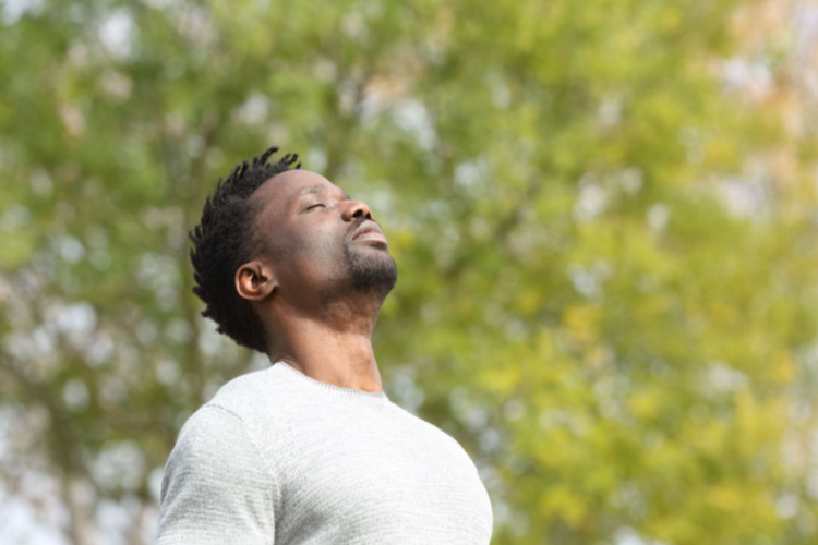 man breathing deeply fresh air in a park a sunny day with a green tree in the background