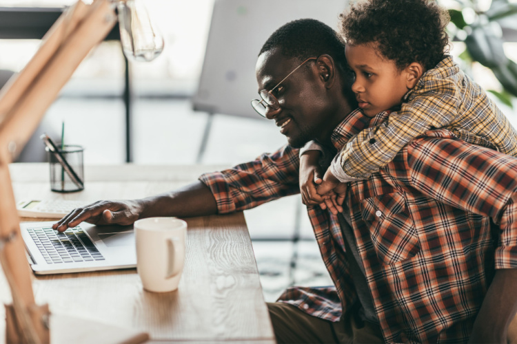side view of smiling african-american father and son using laptop in office