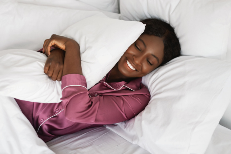 lady embracing pillow smiling with eyes closed lying in bed