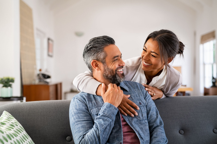 hugging her husband on the couch from behind in the living room.
