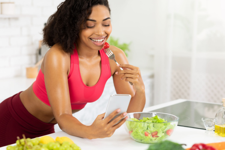 woman eating salad at hone in kitchen, leaning on table