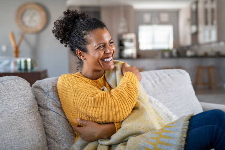 woman sitting on couch wrapped under blanket and laughing.