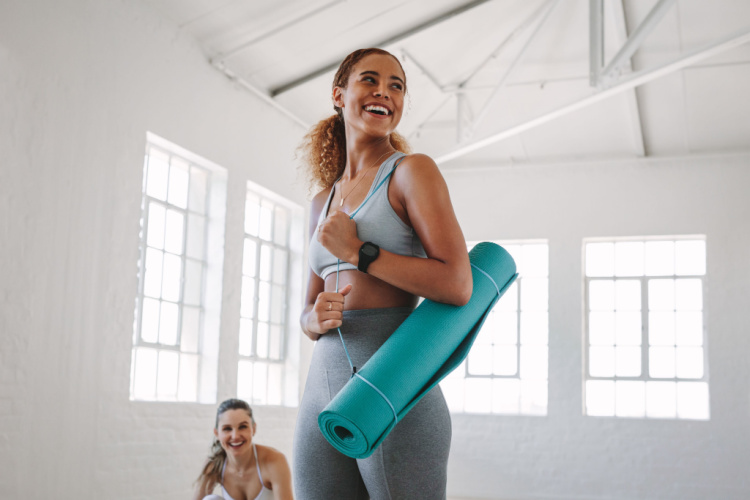 woman standing in a fitness studio carrying a yoga mat.